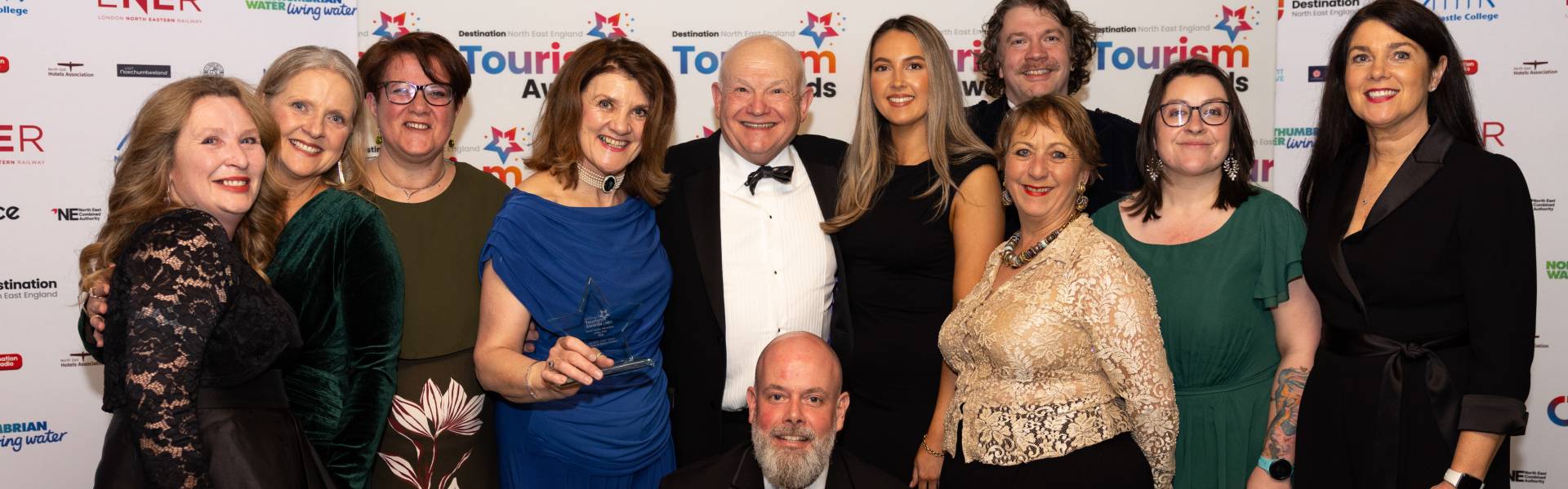 Group of tourism and hospitality industry representatives posing with an award at the North East England Tourism Awards, standing in front of a branded event backdrop.
