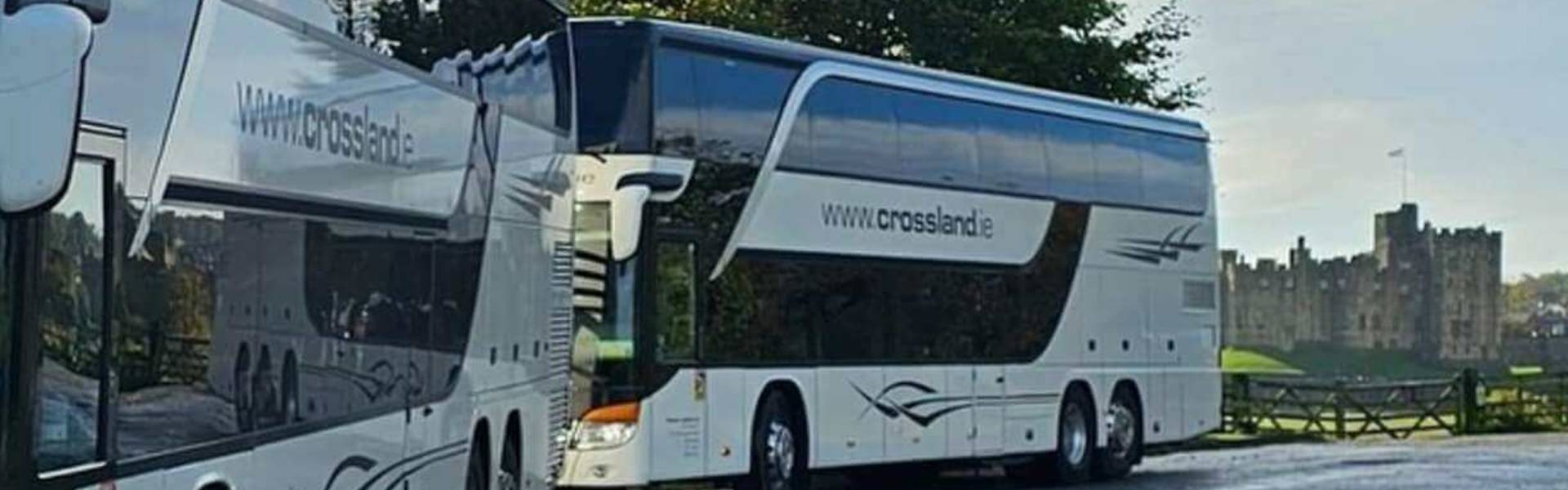 White touring coach parked with a view of Alnwick Castle in the background, representing group travel and coach tourism in the county.